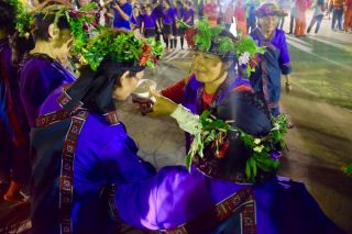 每年農曆9月15日舉辦的小林夜祭,是部落一大盛事。族人齊聚公廨前,牽戲(唱歌跳舞)祝禱太祖降臨。圖為神職人員「山豬婆」在為太祖服務,向族人敬酒。(圖片/Mata Taiwan 提供)