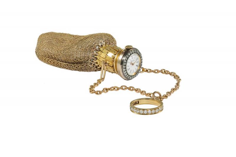 Tiffany附時計的戒環手袋 (1897 - 1903) 黃金、鑽石、黃銅、水晶與琺瑯11.4 x 2.5 cm 這款網狀設計手袋,頸部可伸縮,嵌有一枚時計。手袋與鑲鑽指環之間由兩根鏈條相連。時計錶盤飾有黑色羅馬字母和路易式指針,四周鑲嵌鑽石,並刻有Tiffany品牌標誌,字體與公司創始人Charles Lewis Tiffany的簽名相同。 1897年至1903年的Blue Book出現了帶鑽石錶圈時計的黃金網眼手拿包。Bertha M. White Harrison夫人是這款網眼手袋的原物主,她是商人William Welsh Harrison之妻,她的丈夫與兄弟共同擁有富蘭克林煉糖廠。 他們居住的灰塔莊園位於費城的格倫賽德,占地面積138公頃,建於1893年,共設有40個房間。這座莊園曾一度成為美國最大的私人宅邸。現在,此莊園已併入阿卡迪亞大學校園。