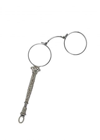 Tiffany 長柄眼鏡 (1890 - 1919) 鉑金、鑽石與玻璃12.4 x 4.3 x 0.9 cm 這款小巧的帶柄眼鏡,手柄上鑲簽了鑽石、兩片鏡片可以組合起來形成一根手柄,做為放大鏡使用。手柄上有個小槓桿結構可以放鬆第二枚鏡片。 長柄眼鏡翻譯自法文單字 “lorgnette”。這種帶有裝飾手柄的手持眼鏡,從定義上是一種眼鏡,但其裝飾作用大於本身的功能。 不同於歌劇眼鏡,女性通常自在白天使用長柄眼鏡,進行閱讀與書寫,其作用與男士的單片眼鏡類似。這種形式的產品最早收錄在1892年的Blue Book中,但類似帶有 “快速鬆脫彈簧” 的眼鏡直到1913年才在Blue Book中出現。